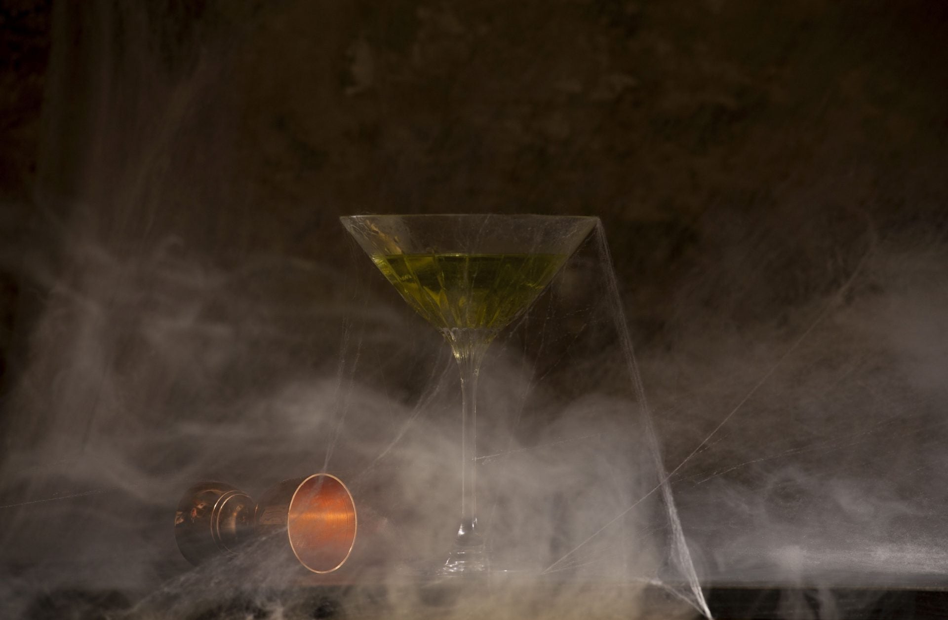 Forgotten Drinks Tasting – Cocktailglas mit grünem Drink, umhüllt von Spinnweben und Nebel, dunkle Atmosphäre.